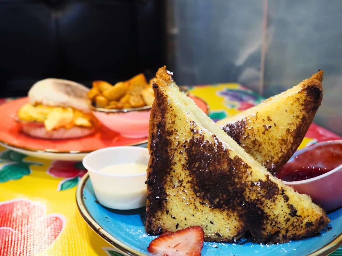 Stuffed french toast with strawberry jam and icing with a breakfast sandwich and home fries on another plate